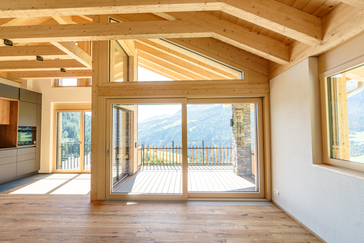 Wohnraum im Dachgeschoss mit sichtbarer Holzkonstruktion, Blick durch die Fenstertüren auf Terrasse und Berge