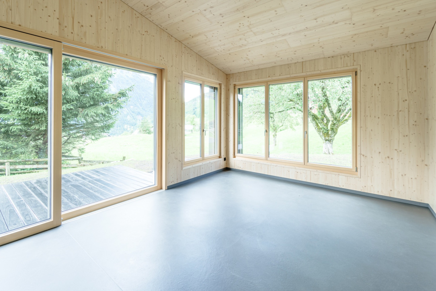 Wohnzimmer mit Fensterfront zur Terrasse und Eckfenstern zur Wiese